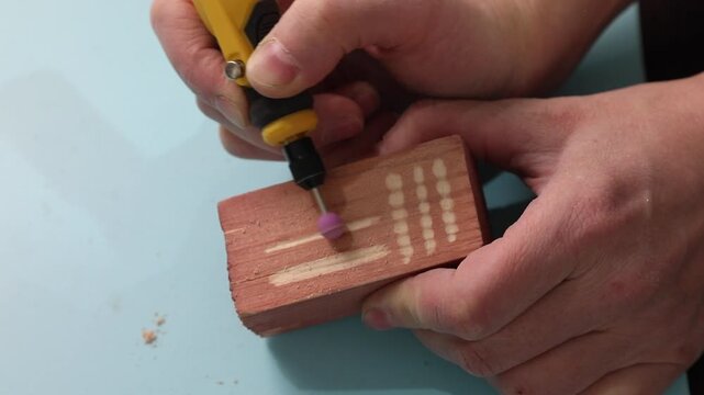Man using hand engraving tool with ceramic tip on painted wooden block. Woodworking process with rotary machine for craft project design.