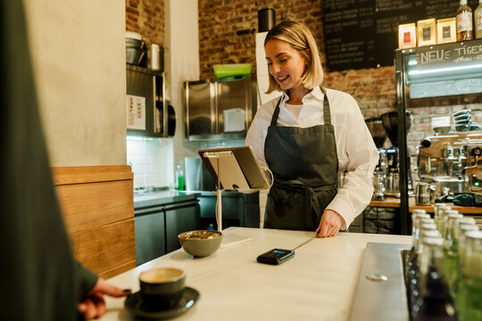 Barista with apron at digital register serving coffee in bistro