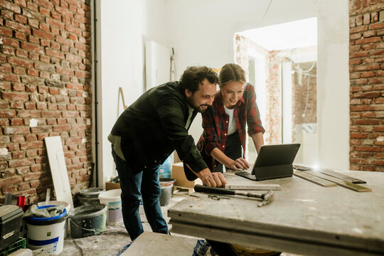 Couple planning home renovation on construction site using laptop