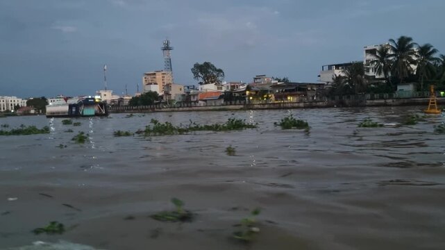 Passenger view of Can Tho&rsquo;s waterfront from a boat on the Hau (Bassac) River, with the riverside promenade visible in soft, overcast early morning light, Vietnam