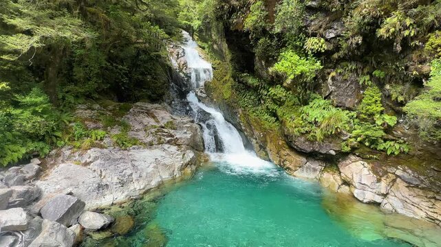 Christie Falls, a crystal-clear turquoise waterfall in Fiordland National Park, New Zealand. Towering cliffs, lush forest, and sparkling waters create a breathtaking alpine scene.