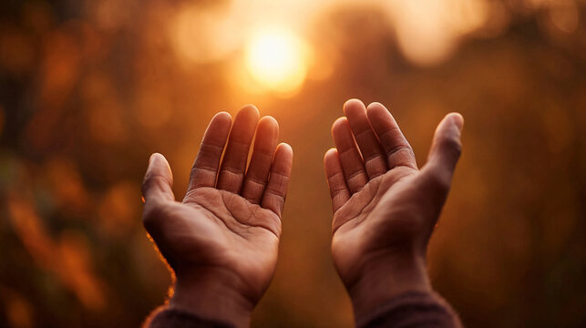Human hands open with palms up in silhouette against a golden, warm sunset or sunrise sky, symbolizing hope, spirituality, and prayer in nature