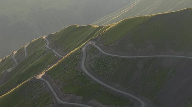 Aerial view of Alazani pass mountains with winding dirt roads, highlighting the contrast between green slopes and rugged terrain, Chala, Tusheti, Georgia.