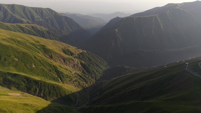 Aerial view of the Alazani pass showing green mountains, a winding path, and a valley, with shadows creating contrast, Chala, Tusheti, Georgia.