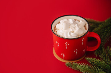 Red mug with hot drink and whipped cream on a red background, cozy holiday mood.