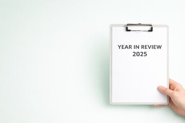 Clipboard with Year in Review 2025 text held by a hand on light background
