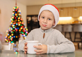 Child drinking from a mug with glowing holiday lights in the background.