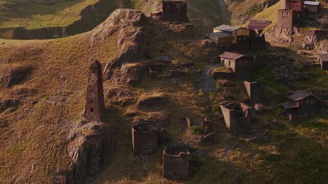 Aerial view of the ancient stone towers in the village of Kvavlo, standing proudly amidst the rugged terrain and golden hues of the mountains, Dartlo, Tusheti, Georgia.