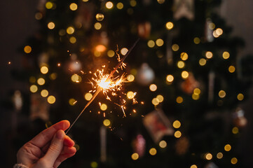 Hand holding a sparkler against blurred festive holiday lights background.