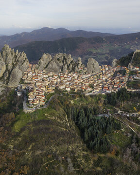 Aerial view of a village nestled amongst jagged peaks and verdant valleys, the warm terracotta roofs contrast against the cool grey stone, Pietrapertosa, Basilicata, Italy.