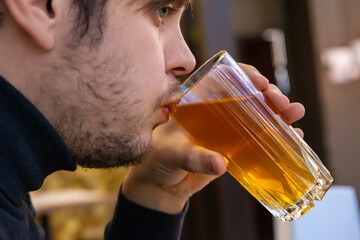 Young man drinking dried fruit compote from glass mug. Healthy drink for refreshment and hydration.