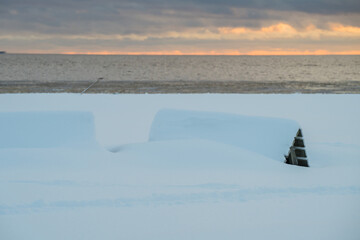 View of snow-covered objects under a moody sky at the baltic sea with a distant warm glow in the horizon, Parnu, Estonia.