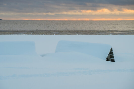 View of snow-covered objects under a moody sky at the baltic sea with a distant warm glow in the horizon, Parnu, Estonia.