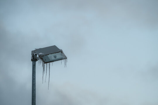 View of icicles hanging from a cold, metallic street lamp against a muted, overcast sky, creating a stark contrast in Parnu, Estonia.