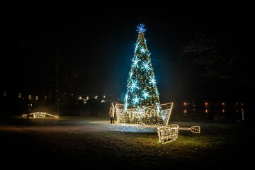 View of a shimmering Christmas tree crafted into a boat shape, glowing brightly against the dark night sky, a festive beacon, Trakai, Lithuania.