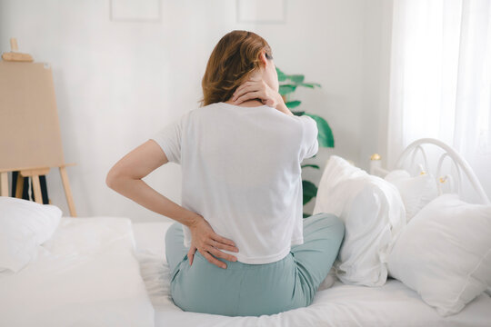 The young woman experienced body aches while sitting on the bed. She felt pain and stiffness in her shoulders, neck, and back, along with muscle spasms and general discomfort.