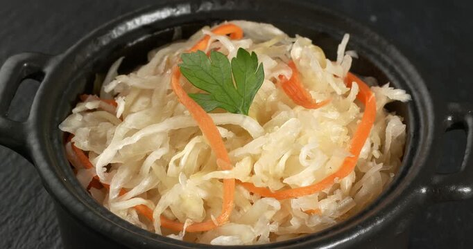 Bowl of fermented cabbage with parsley and carrots, sauerkraut, sauer kraut, a healthy vegan crunchy probiotic. Close-up footage on the rotating table.