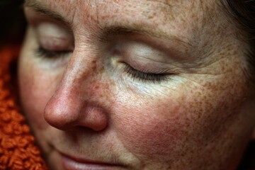 A woman is resting with her eyes closed, showing her freckles and relaxed expression in a cozy environment