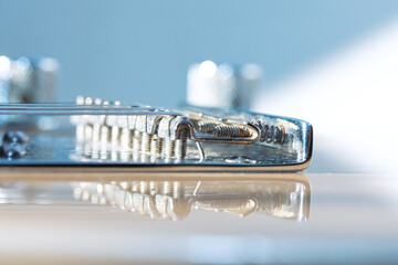 Electric guitar bridge reveals coiled strings anchored to gleaming metal. Reflections highlight instrument mechanical precision and musical craftsmanship. String saddles and guitar bridge assembly