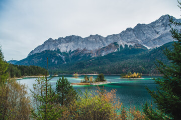 View of emerald waters reflecting the sky and towering mountains, with islands adorned with trees in autumn colors, Garmisch-Partenkirchen, Bavaria, Germany.