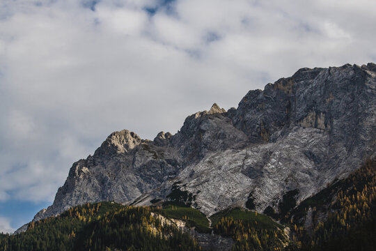 View of jagged mountain peaks rise against a backdrop of soft, billowing clouds, their rocky faces etched with shadows and light, Garmisch-Partenkirchen, Bavaria, Germany.