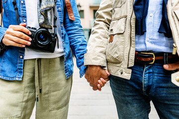 Mature couple walking together holding hands, exploring a city, with one person carrying a camera, symbolizing travel, love, and life partnership in retirement