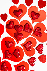 Red heart shape cutouts with glitter details on a white background. Concept of love, romance, and celebration for Valentines Day.