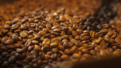 Close-up of a pile of medium-dark roasted coffee beans. The beans have a matte texture and are illuminated by warm light, suggesting freshness and aroma.