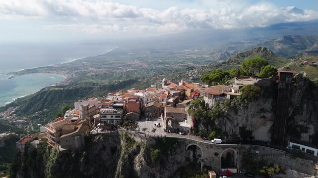 Drone aerial view of Castelmola, Sicily, with mountains in the background, cinematic 4K 60FPS footage showcasing historic hillside village, rooftops, and Mediterranean landscape