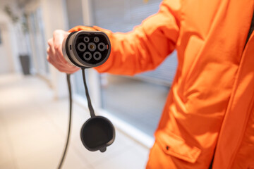 fast charging connector Close-up, electric car charging plug held man in orange jacket, connection point for DC electric vehicle refueling, EV technology, future mobility against charging station
