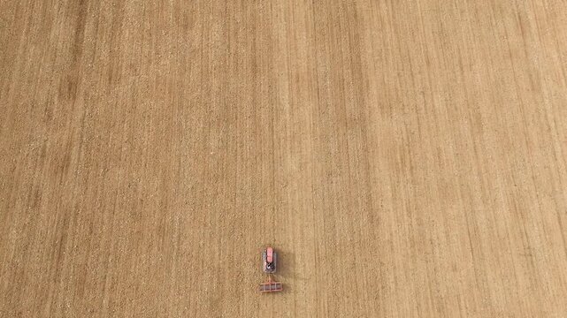 Vintage crawled tractor is leveling plowed soil in a vast, brown field, showcasing agricultural work and sustainable farming practices in the rural Italian landscape