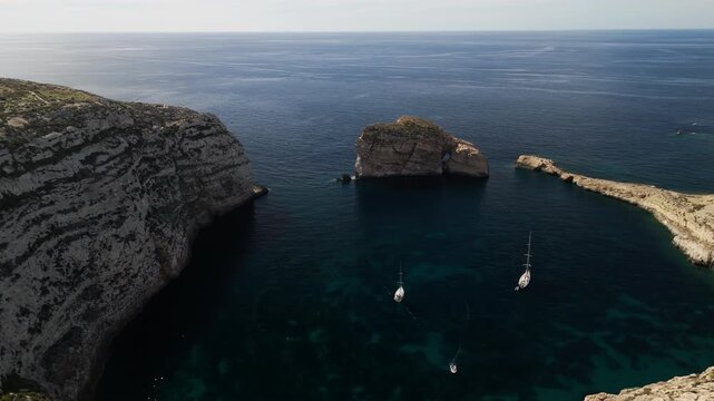 rone aerial view of sailboat anchored in protected bay at Dwejra, Gozo, Malta, cinematic 4K 60FPS footage showcasing dramatic limestone cliffs and Mediterranean seascape
