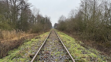 Fototapeta premium Old and degraded railway line before modernization, with rusty rails and worn wooden sleepers. Abandoned and neglected tracks stretching into the distance, symbolizing decay.