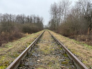 Fototapeta premium Old and degraded railway line before modernization, with rusty rails and worn wooden sleepers. Abandoned and neglected tracks stretching into the distance, symbolizing decay.