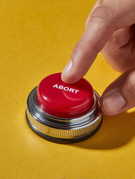 Hand pressing a red emergency abort button on yellow background.