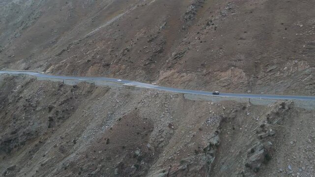 Aerial view of cars traversing a winding road carved into the rugged, rocky mountain terrain, showcasing the stark beauty, Besal, Khyber Pakhtunkhwa, Pakistan.