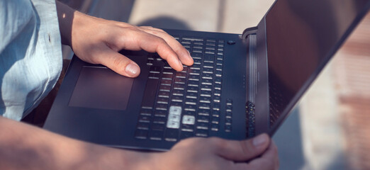 Man is typing, working on a laptop, hands on a keyboard closeup