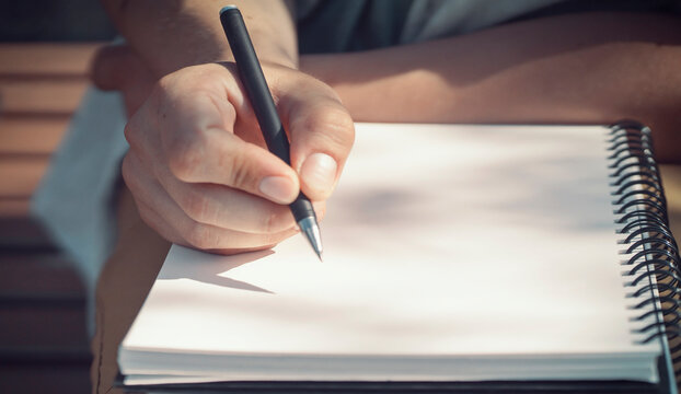 A male hand holds a pen and writes in a sketchbook, notepad closeup.