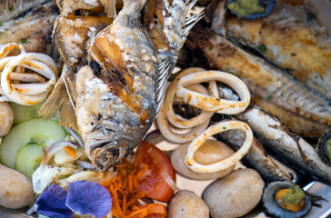 A grilled fish mix plate with various types of fish, seafood, scallops and squid rings.