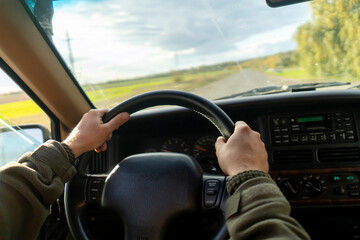 A man is driving his car on the road at sunset.
