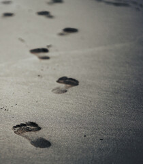 A black volcanic sand on a beach closeup with a person footprints.