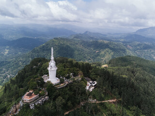 Aerial view of the white Ambuluwawa Tower located on a mountain peak surrounded by lush greenery, in Kandy, Sri Lanka