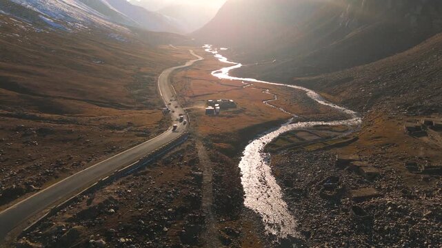 Aerial view of a road alongside a stream winding through a valley, the landscape marked by earthy tones and sparse greenery, Gittidas, Khyber Pakhtunkhwa, Pakistan.