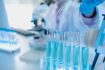 Two female scientists in white lab coats working together in a bright laboratory with microscopes, glassware, and blue test tubes, representing teamwork and modern scientific research environment.