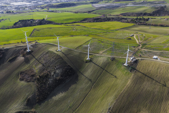Aerial view of wind turbines gracefully standing along the rolling hills, a symphony of white against the patchwork of green and brown, Potenza, Basilicata, Italy.