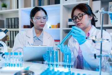 Two chemists in white lab coats working together in a modern laboratory surrounded by scientific equipment, computers, and glassware, representing teamwork in scientific research.
