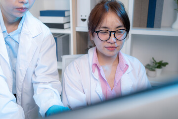 Two chemists in white lab coats working together in a modern laboratory surrounded by scientific equipment, computers, and glassware, representing teamwork in scientific research.