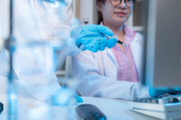 Two chemists in white lab coats working together in a modern laboratory surrounded by scientific equipment, computers, and glassware, representing teamwork in scientific research.