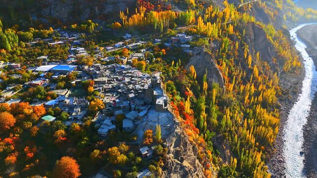 Aerial view of Baltit Fort perched atop a hill, surrounded by autumn trees and a winding river creating a scenic landscape, Hunza, Gilgit Baltistan, Pakistan.