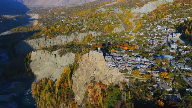 Aerial view of Baltit Fort perched atop a rugged mountain, surrounded by autumn foliage and a clustered village, Hunza, Gilgit Baltistan, Pakistan.